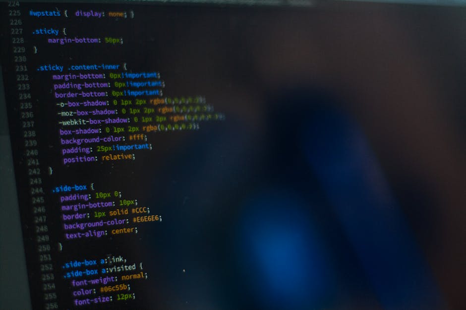 A close-up view of a computer screen displaying lines of HTML and CSS code in various colors, including blue, green, yellow, and purple, on a dark background. The code consists of tags, properties, an